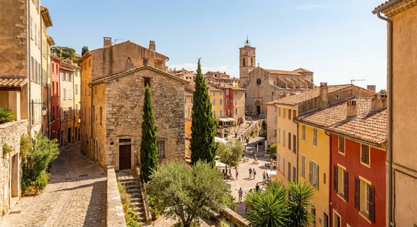 Photographie réaliste de la ville de Grasse, France, montrant des éléments architecturaux et urbains caractéristiques : vue du centre-ville historique avec ses ruelles typiques provençales, ses bâtiments en pierre, ses façades colorées ou terracotta, et ses toits de tuiles. La photo peut inclure des éléments emblématiques comme la cathédrale Notre-Dame-du-Puy, les places publiques du centre-ville, ou une perspective des quartiers reconnaissables de Grasse. La photo doit être prise de jour, bien éclairée, avec une qualité professionnelle, sans texte ni logo visible. Elle doit représenter distinctement Grasse et son caractère provençal pour se démarquer visuellement des images côtières de Cannes, Antibes et Nice.