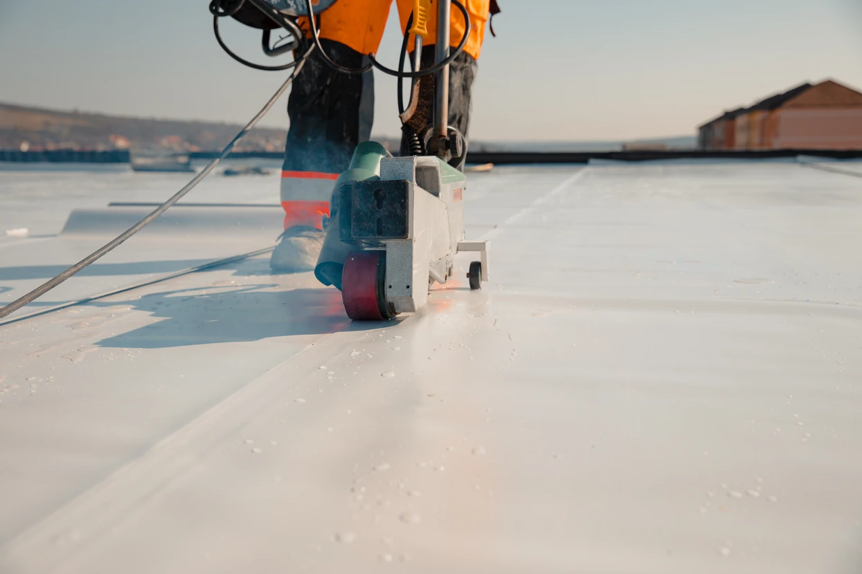 Chantier extérieur sur toiture membrane blanche, ouvrier en équipement de sécurité utilisant une soudeuse thermoplastique automatique