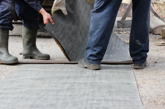 Ouvrier en combinaison de protection blanche appliquant un revêtement d'étanchéité sur une toiture-terrasse avec un rouleau à manche télescopique
