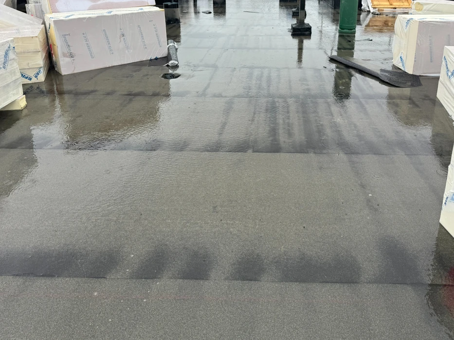 Toiture-terrasse plate recouverte d'eau stagnante après une pluie, révélant des problèmes de drainage