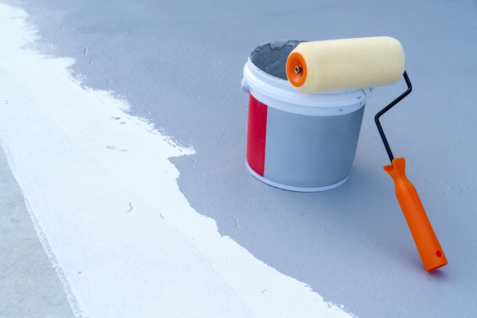 Ouvrier en combinaison de protection blanche appliquant un revêtement d'étanchéité sur une toiture-terrasse avec un rouleau à manche télescopique