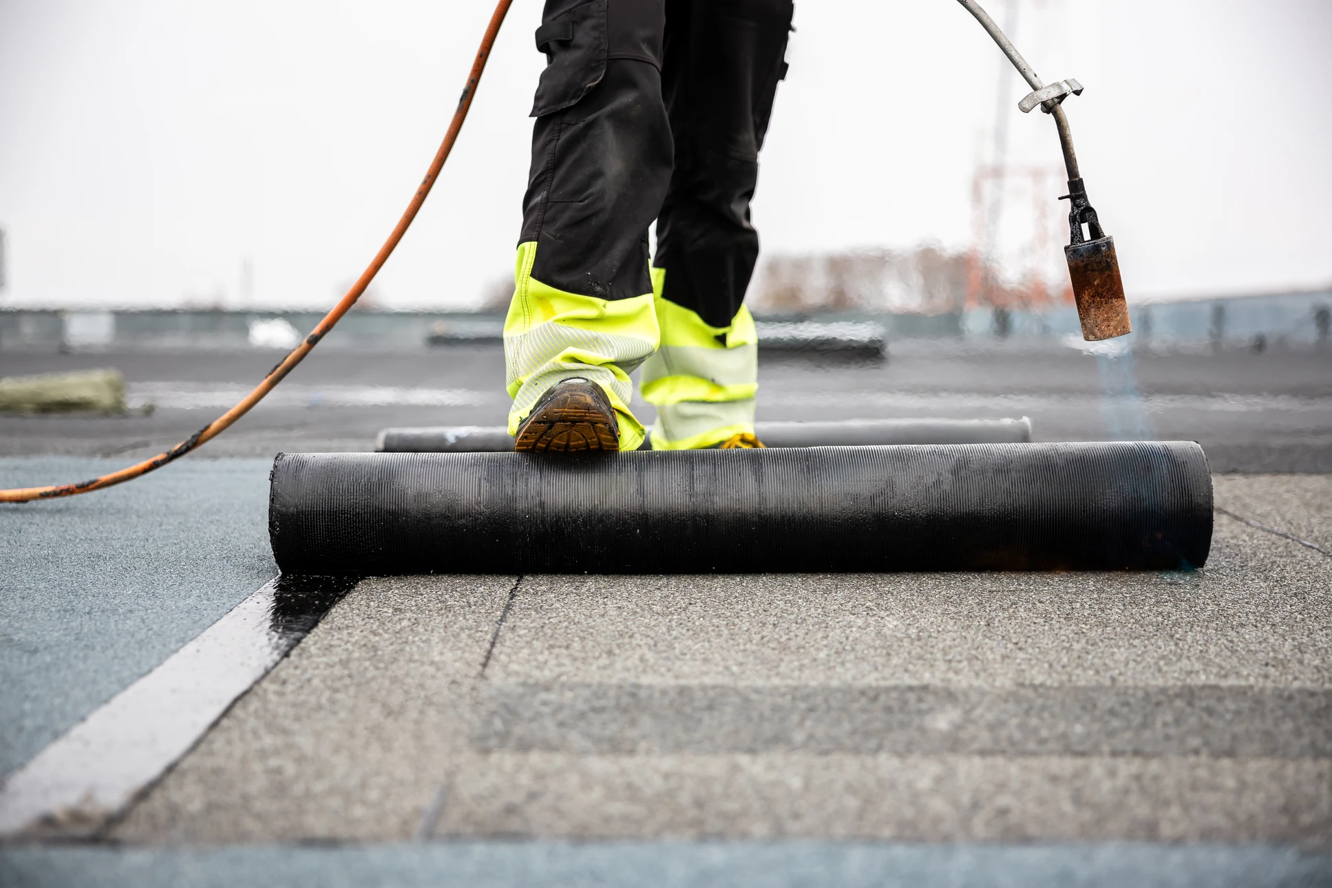 Ouvrier appliquant un revêtement d'étanchéité liquide sur une toiture-terrasse en béton à l'aide d'un rouleau à manche télescopique bleu